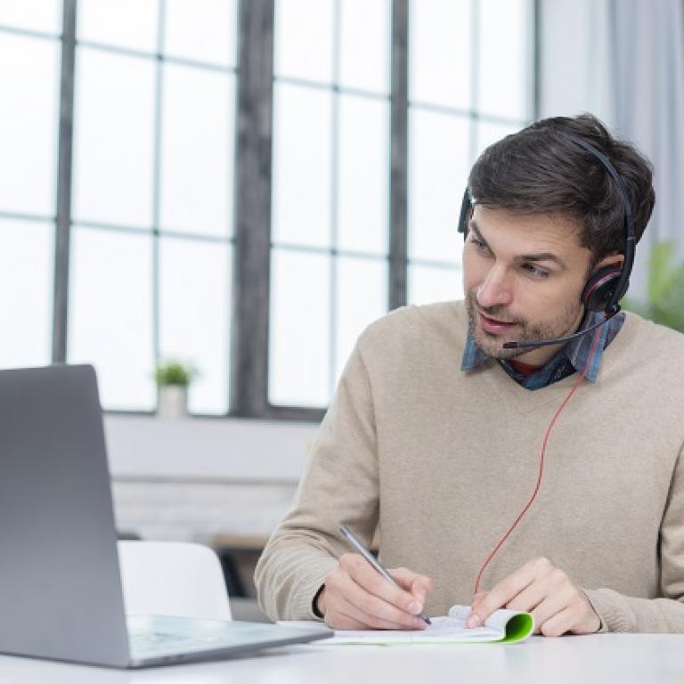 Man with a headphone following a videoconference on his laptop