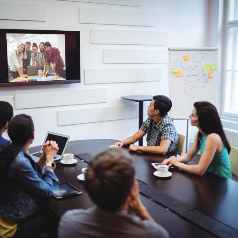 verschillende personen die via tv-scherm in vergaderzaal online vergaderen
